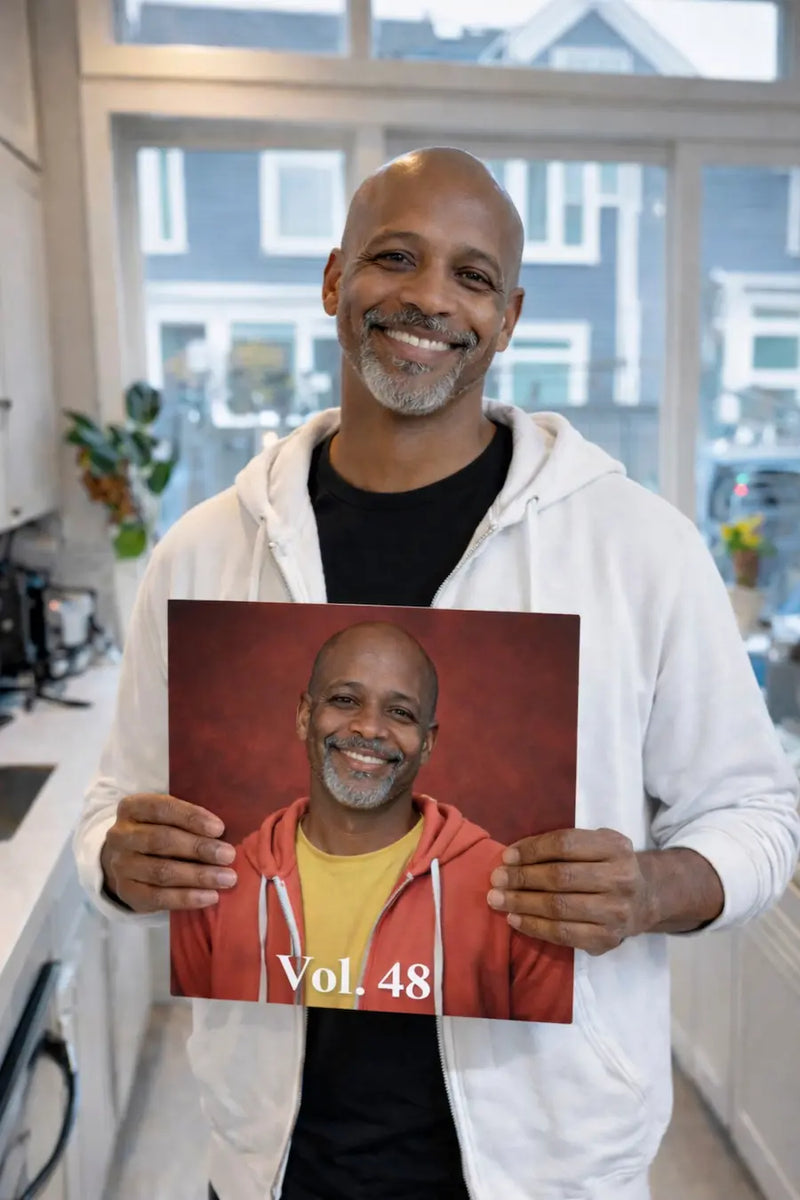 A smiling man holding his custom vinyl record birthday gift in a bright home interior