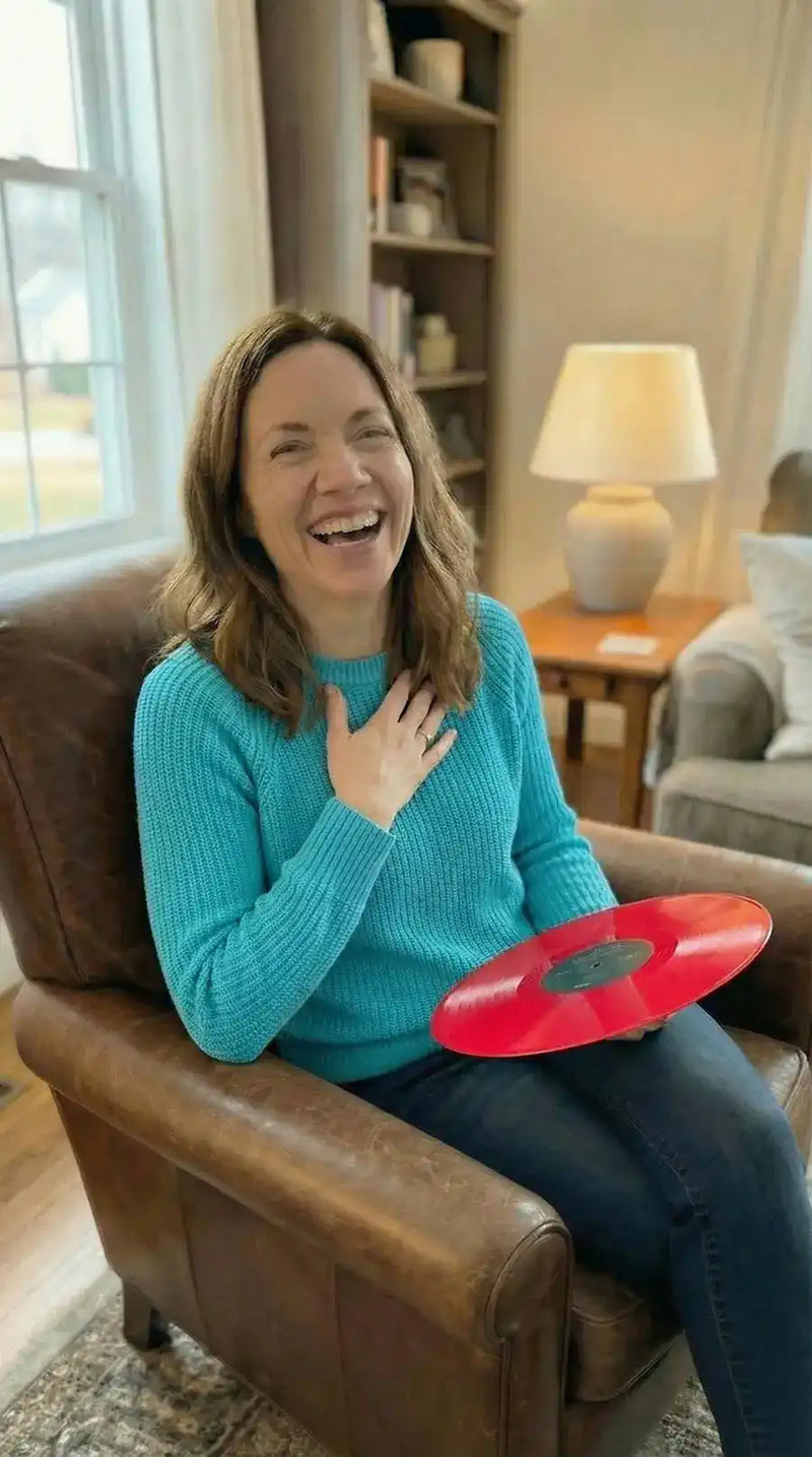 A happy woman sitting in an armchair holding a red personalized vinyl record gift