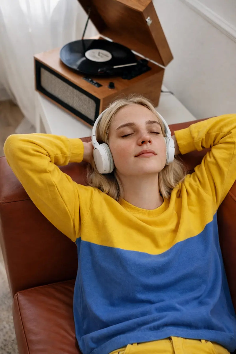A happy woman in a blue and yellow sweater relaxing on a chair while listening to her custom personalized vinyl record